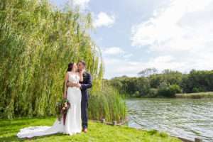 Bride & Groom kissing on the riverbank at The Boat House in Norfolk with the willow tree behind them